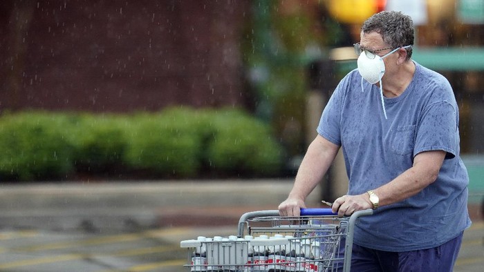 A shopper wears a mask as he pushes a grocery cart in the rain Thursday, June 25, 2020, in Houston. Texas Gov. Greg Abbott said Wednesday that the state is facing a massive outbreak in the coronavirus pandemic and that some new local restrictions may be needed to protect hospital space for new patients. (AP Photo/David J. Phillip)