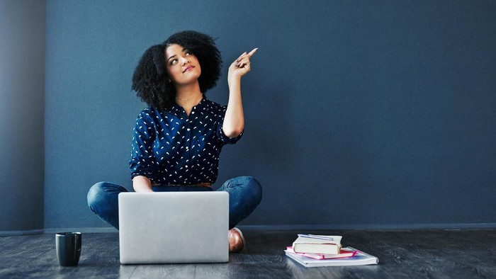 Studio shot of an attractive young woman looking thoughtful while using a laptop against a blue background