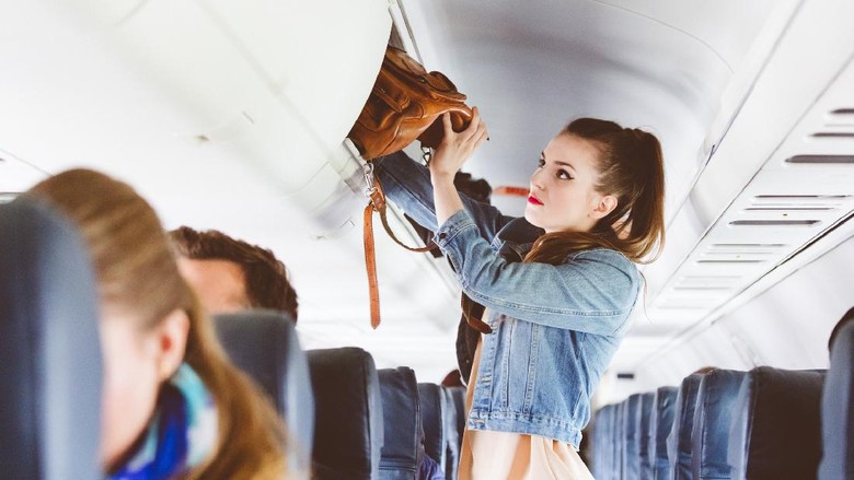 Female passenger storing handbag in overhead locker in airplane. Young woman in the cabin storing hand luggage in the overhead locker.