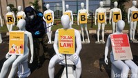 Para aktivis tetap memberlakukan protokol kesehatan dengan menyemprotkan disinfektan terhadap manekin yang dijejerkan di depang gedung DPR.