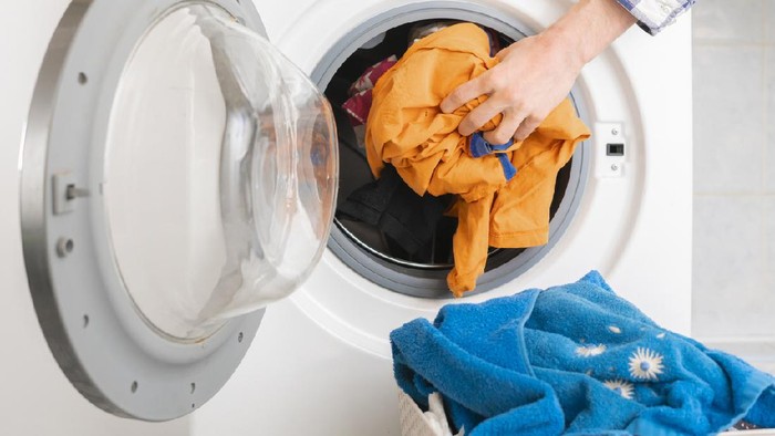 persons hand put dirty clothes in the washing machine