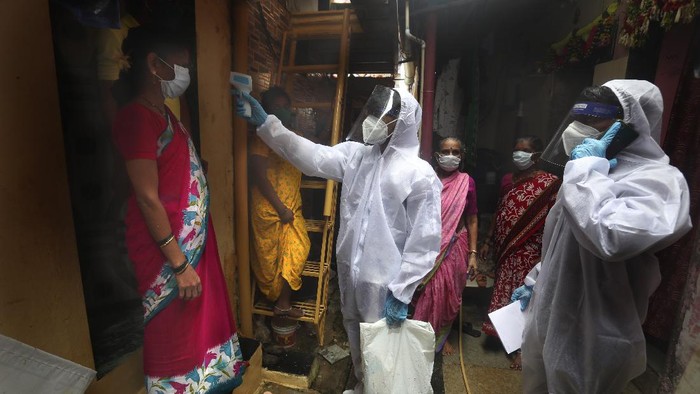 A health worker checks the body temperature of a resident, as others await their turn during a free medical checkup in a slum in Mumbai, India, Sunday, June 28, 2020. India is the fourth hardest-hit country by the COVID-19 pandemic in the world after the U.S., Russia and Brazil. (AP Photo/Rafiq Maqbool)