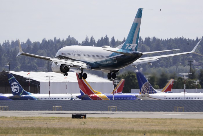 A Boeing 737 MAX jet heads to a landing and past grounded 737 MAX jets behind at Boeing Field following a test flight Monday, June 29, 2020, in Seattle. The jet took off from Boeing Field earlier in the day, the start of three days of re-certification test flights that mark a step toward returning the aircraft to passenger service. The Federal Aviation Administration test flights over the next three days will evaluate Boeings proposed changes to the automated flight control system on the MAX, a system that activated erroneously on two flights that crashed, killing 346 people. (AP Photo/Elaine Thompson)