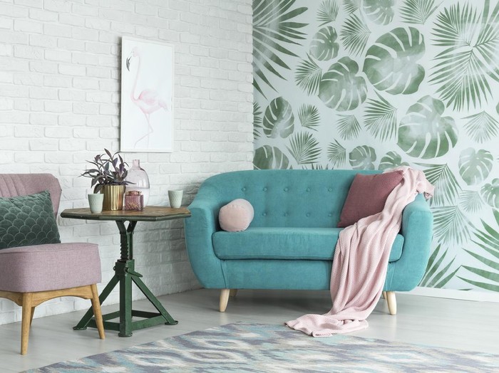 Green table with plant between pink chair and blue sofa in floral living room with wallpaper and poster