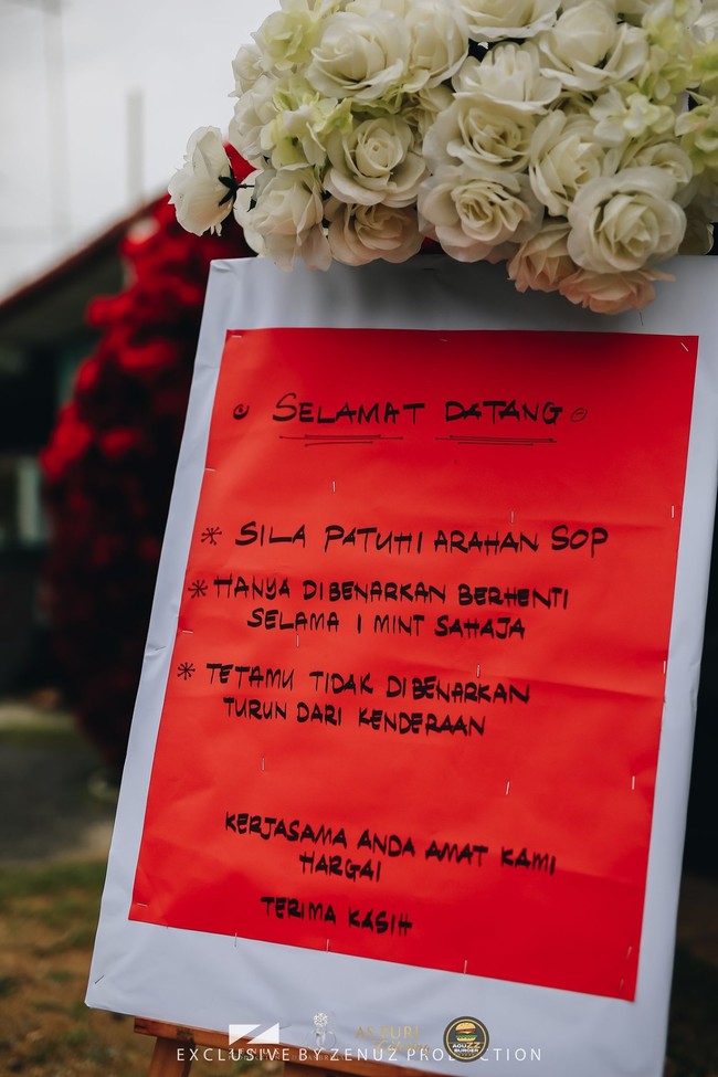 Sebelum memasuki area pelaminan, terpasang papan pengumuman yang memberitahukan SOP kondangan. Dalam SOP tersebut tertulis tamu undangan hanya diizinkan berhenti selama satu menit untuk memberi ucapan selamat pada kedua mempelai. Para tamu juga tidak diizinkan turun dari kendaraannya. Foto: Dok. Zenuz Production