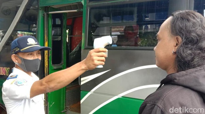 Petugas memeriksa suhu tubuh penumpang bus