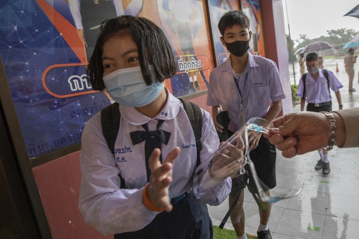 Virus Outbreak Thailand Schools A teacher in protective gear holds class with students seated at partitioned desks at Samkhok School in Pathum Thani, outside Bangkok, Wednesday, July 1, 2020. Thailand has begun a fifth phase of relaxations of COVID-19 restrictions, allowing the reopening of schools and high-risk entertainment venues such as pubs and massage parlors that had been shut since mid-March. (AP Photo/Sakchai Lalit)