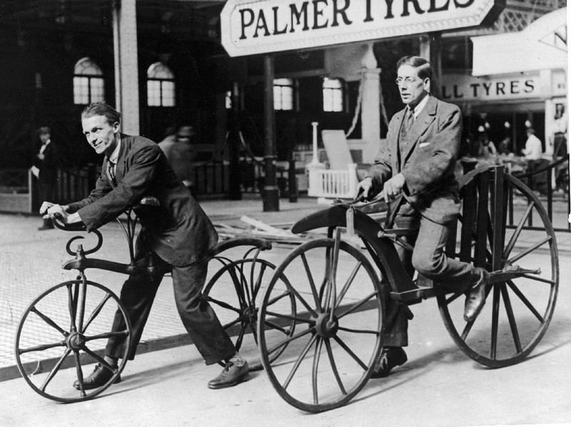 Two men (L-R) ride on early bicycles. The Hobby Horse was invented by Karl Von Drais in 1818. In 1863, a French coachbuilder added cranks and pedals and invented the 'boneshaker', circa 19th century.