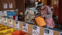 Dua orang warga sedang mengelompokkan sampah rumah tangga mereka ke dalam keranjang-keranjang yang telah disediakan.