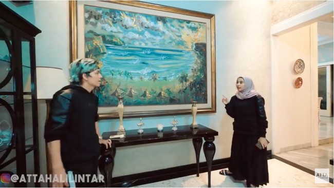 Masuk ke rumah, langsung disambut ruang tamu yang luas. Ruangan ini dipermanis dengan lukisan dan hiasan kaligrafi. Bella lalu menceritakan asal muasal lukisan besar yang menghiasi salah satu sudut ruang tamunya. Jadi ini aku dikasih sama pelukis dari Bali. Namanya Pak Made. Orangnya baik banget, puji Laudya. (Foto: YouTube/Atta Halilintar)