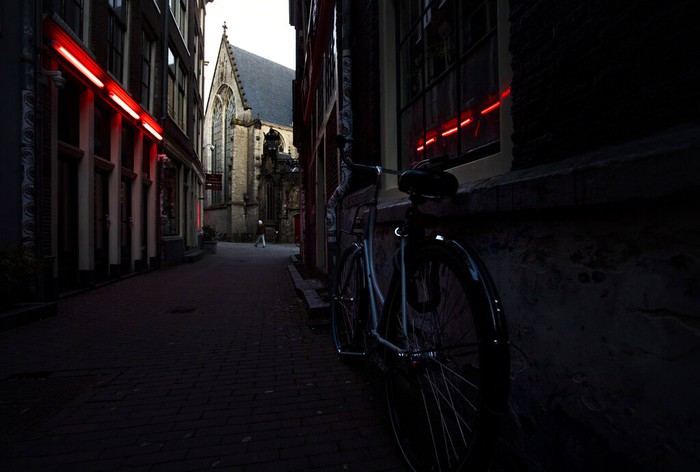Virus Outbreak Netherlands Red Light District Oude Kerk, or Old Church, is reflected in the window of the PIC, Prostitution Information Center, as sex workers welcomed clients again in the Red Light District in Amsterdam, Netherlands, Wednesday, July 1, 2020. It wasn't quite business as usual as the capital's Red Light District emerged from coronavirus lockdown, but it was as close as it has been since the pandemic slammed the brakes on the world's oldest profession. (AP Photo/Peter Dejong)