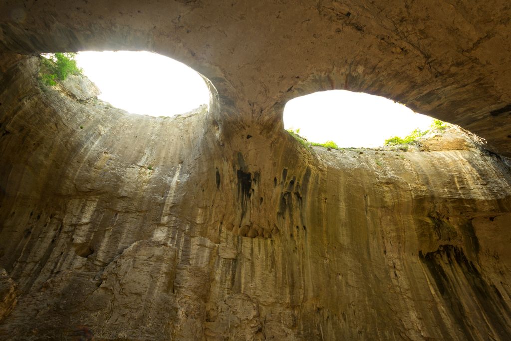 Young Woman with rise arms looks up to the eyes in the rocks. 