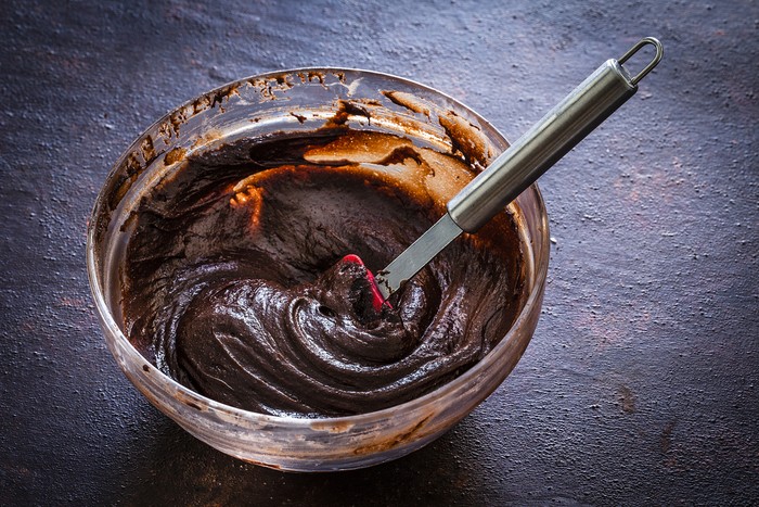 High angle view of a mixing bowl filled with melting chocolate mix shot on dark brown rustic kitchen table. A spatula is inside the mixing bowl. Predominant color is brown. Low key DSRL studio photo taken with Canon EOS 5D Mk II and Canon EF 100mm f/2.8L Macro IS USM.