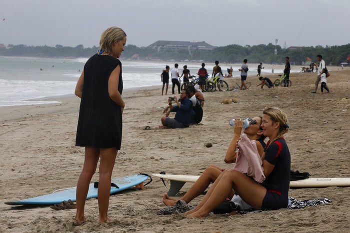 Orang-orang menyaksikan matahari terbit di sebuah pantai di Bali, Indonesia, Kamis (9/7/2020). Pulau resort di Bali dibuka kembali setelah tiga bulan terkunci akibat pandemi virus Corona pada Kamis ini. Pembukaan tahap pertama ini hanya untuk wisatawan dan penduduk lokal serta sebagian turis asing yang terdampar untuk melanjutkan kegiatan publik sebelum kembali dibuka untuk kedatangan orang asing pada September mendatang. (Foto AP / Firdia Lisnawati)