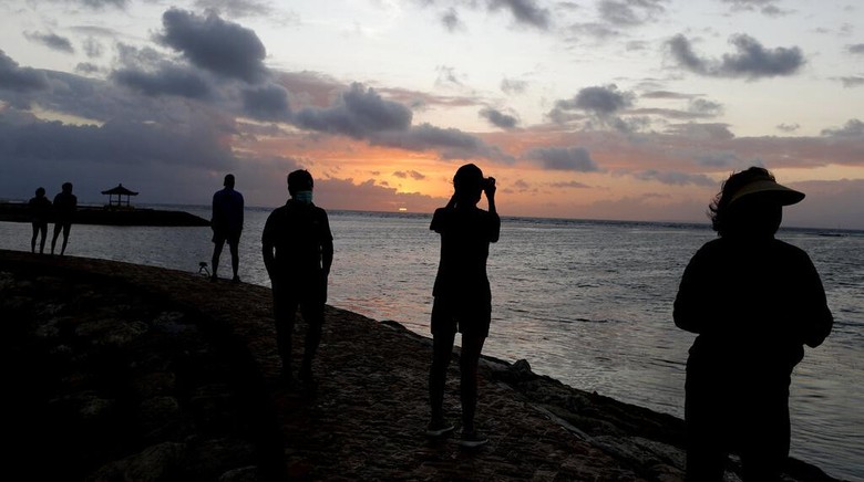 Bali kembali di buka untuk Umum Orang-orang menyaksikan matahari terbit di sebuah pantai di Bali, Indonesia, Kamis (9/7/2020). Pulau resort di Bali dibuka kembali setelah tiga bulan terkunci akibat pandemi virus Corona pada Kamis ini. Pembukaan tahap pertama ini hanya untuk wisatawan dan penduduk lokal serta sebagian turis asing yang terdampar untuk melanjutkan kegiatan publik sebelum kembali dibuka untuk kedatangan orang asing pada September mendatang. (Foto AP / Firdia Lisnawati)