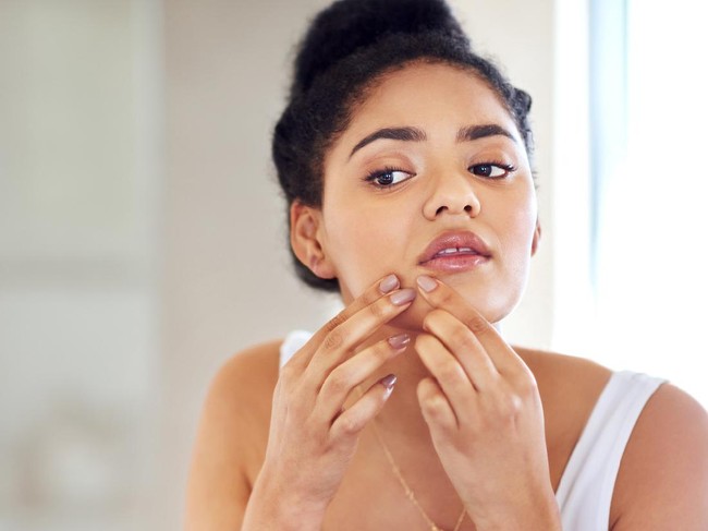 Shot of a young woman squeezing a pimple on her face in the bathroom