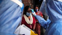 Seorang petugas kesehatan memeriksa suhu seorang wanita menggunakan termometer elektronik untuk memeriksa suhu tubuh di daerah kumuh di Mumbai, India.