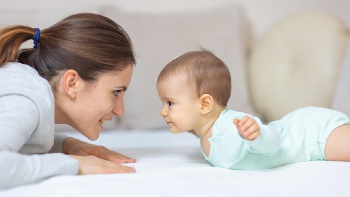 Mother and 7 months old baby doing exercises on the bed and learning to crawl