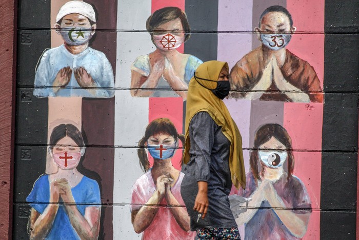 Warga melintas di dekat mural bergambar simbol orang berdoa menggunakan masker yang mewakili umat beragama di Indonesia di kawasan Juanda, Kota Depok, Jawa Barat, Kamis (18/6/2020). Mural yang dibuat oleh warga itu bertujuan untuk memberikan edukasi kepada masyarakat untuk menggunakan masker sebagai salah satu  pencegahan dan penyebaran COVID-19. ANTARA FOTO/Yulius Satria Wijaya/aww.