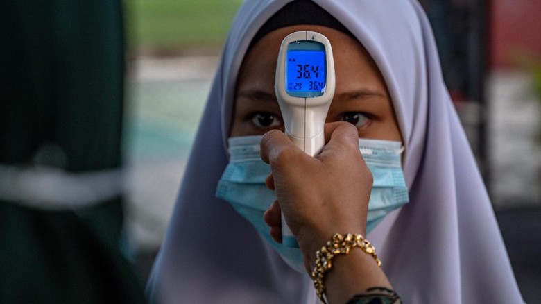 A high school teacher checks the temperature of a student on the first day after being reopened following restrictions to halt the spread of the COVID-19 coronavirus in Kuala Lumpur on June 24, 2020. (Photo by Mohd RASFAN / AFP)