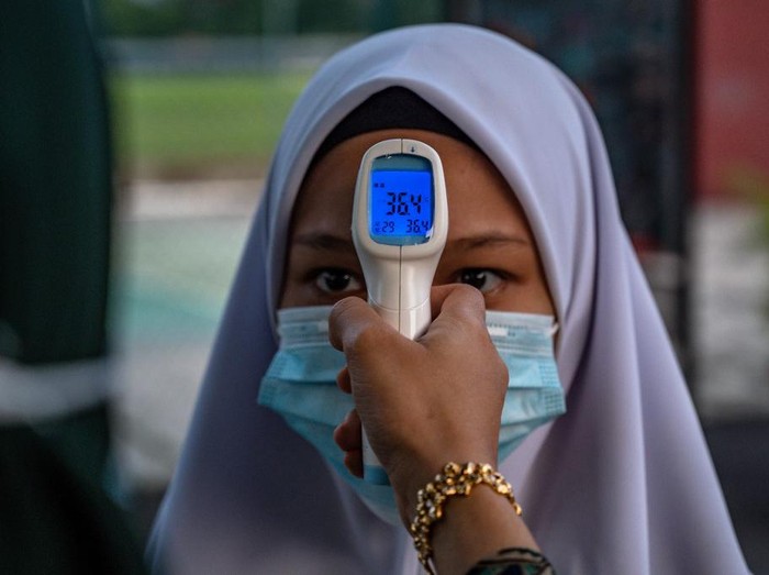 A high school teacher checks the temperature of a student on the first day after being reopened following restrictions to halt the spread of the COVID-19 coronavirus in Kuala Lumpur on June 24, 2020. (Photo by Mohd RASFAN / AFP)