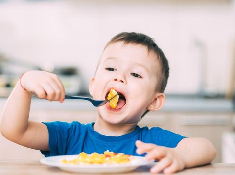 a child in a t-shirt in the kitchen eating an omelet, a fork