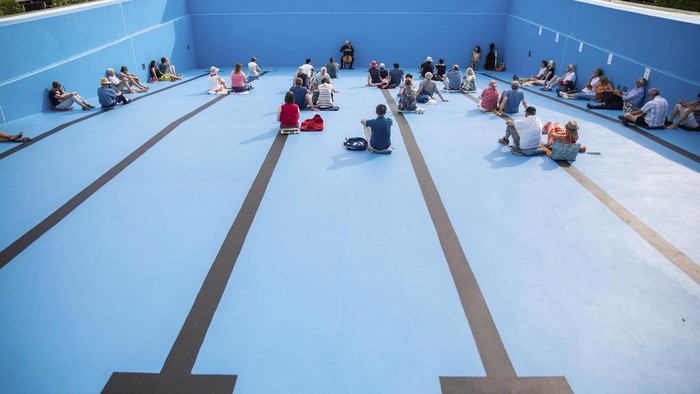 Visitors watch a cello concert by J'rgen Gerlinger performed in an empty outdoor swimming pool, in Entringen, Germany, Sunday July 19, 2020.  J'rgen Gerlinger is a member of the Bayreuth Festival Orchestra.  (Christoph Schmidt/dpa via AP)