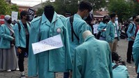 Tak hanya poster, dalam aksi itu tampak pula sebuah kertas bertuliskan B.U. Rp 185.000 dikalungkan pada almamater UNS di tengah aksi para mahasiswa tersebut. Istimewa/ Dok. Aliansi Mahasiswa UNS Bergerak.