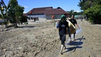 Warga melewati material lumpur sambil membawa barang miliknya di Desa Radda, Kabupaten Luwu Utara.