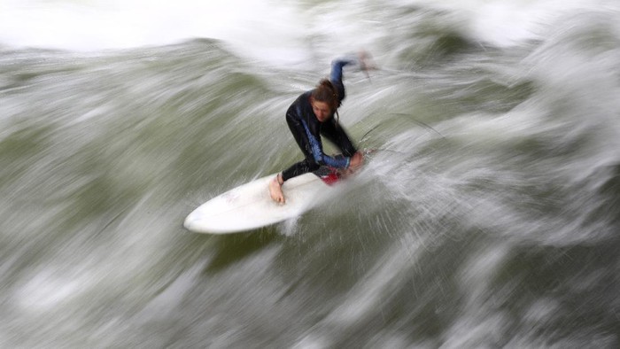 Sejumlah peselancar di Jerman menghabiskan waktu untuk beraksi memecah ombak buatan di Sungai Eisbach. Nah, seperti apa keseruannya?