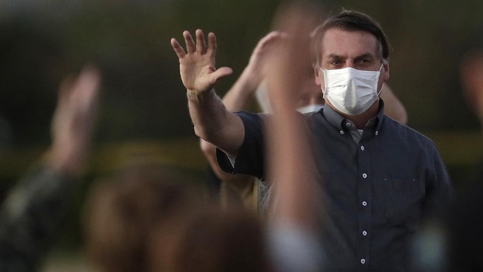 Brazils President Jair Bolsonaro who is infected with COVID-19, wears a protective face mask as he waves to supporters during a Brazilian flag retreat ceremony outside his official residence the Alvorada Palace, in Brasilia, Brazil, Monday, July 20, 2020. (AP Photo/Eraldo Peres)