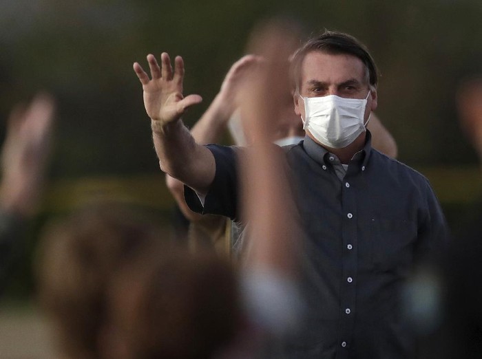 Brazils President Jair Bolsonaro who is infected with COVID-19, wears a protective face mask as he waves to supporters during a Brazilian flag retreat ceremony outside his official residence the Alvorada Palace, in Brasilia, Brazil, Monday, July 20, 2020. (AP Photo/Eraldo Peres)