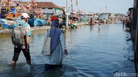 Petugas nekat menerabas genangan banjir rob atau air pasang laut yang tak kunjung surut.