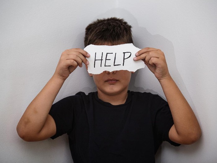 HELP, Teenager with help sign. Boy holding a paper with the inscription. Kid holding sheet of paper with word HELP on grey wall background.