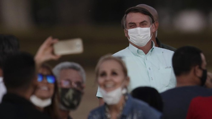 Supporters pose for a selfie as Brazils President Jair Bolsonaro, who is infected with COVID-19, wears a protective face mask while attending a Brazilian flag retreat ceremony outside his official residence the Alvorada Palace, in Brasilia, Brazil, Wednesday, July 22, 2020. Bolsonaro has tested positive for the new coronavirus for the third time, following his July 7 announcement that he had COVID-19, the Brazilian government confirmed. (AP Photo/Eraldo Peres)