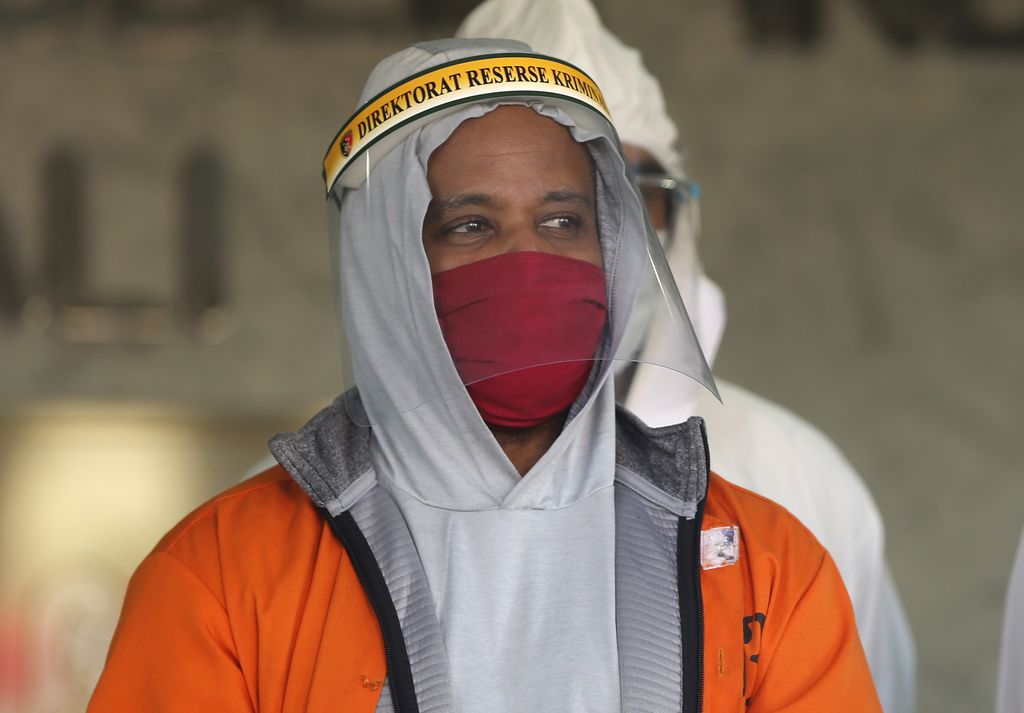U.S. national Marcus Beam, center, wearing protective equipment as precaution against the coronavirus, is flanked by police as he is presented to the media during a press conference at the Regional Police Headquarters in Denpasar, Bali, Indonesia, Friday, July 24, 2020. Authorities on the resort island arrested Beam, an American fugitive accused of investment fraud in the United States involving hundreds of thousands of dollars, police said Friday. The U.S. Securities and Exchange Commission said on its website that Beam, of Woodridge, Illinois, is accused of misappropriating about $500,000 from investors that was supposed to be placed in investment funds. (AP Photo/Firdia Lisnawati)