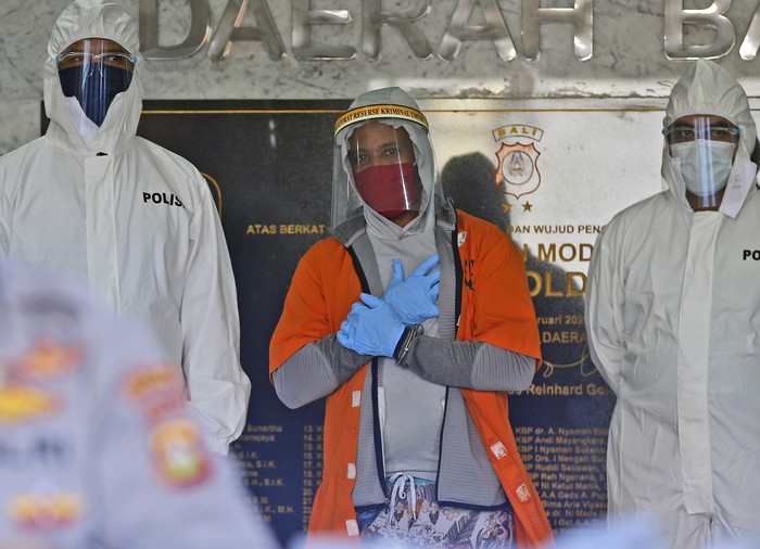 U.S. national Marcus Beam, center, wearing protective equipment as precaution against the coronavirus, is flanked by police as he is presented to the media during a press conference at the Regional Police Headquarters in Denpasar, Bali, Indonesia, Friday, July 24, 2020. Authorities on the resort island arrested Beam, an American fugitive accused of investment fraud in the United States involving hundreds of thousands of dollars, police said Friday. The U.S. Securities and Exchange Commission said on its website that Beam, of Woodridge, Illinois, is accused of misappropriating about $500,000 from investors that was supposed to be placed in investment funds. (AP Photo/Firdia Lisnawati)