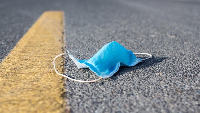 1257393888 Pandemic littering and environmental pollution concept. Blue disposable face mask laying flat next to a road marking.