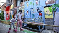Anak-anak bermain dilapangan bulutangkis yang dipenuhi dengan mural bahaya COVID-19 di kawasan Kali Pasir, Cikini, Jakarta Pusat, Senin (27/7/2020).