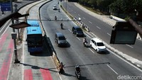 Seorang pedagang berdiri di depan separator busway menanti pembeli.