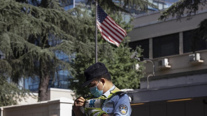 A Chinese police officer adjusts his vest near the U.S. flag flying in the United States Consulate in Chengdu in southwest Chinas Sichuan province on Sunday, July 26, 2020. China ordered the United States on Friday to close its consulate in the western city of Chengdu, ratcheting up a diplomatic conflict at a time when relations have sunk to their lowest level in decades. (AP Photo/Ng Han Guan)