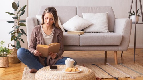 Self education concept. Young woman reading book, sitting on floor at home, panorama, free space