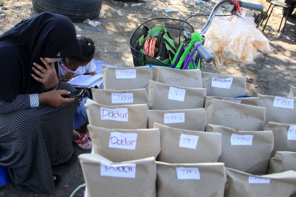 Pelajar kelas VIII MTs Darul Ulum, Sovi Dwi Aprilia (kiri) bersama adiknya, Tri Wahyu, yang masih kelas I SD belajar sambil berjualan nasi bungkus di pinggir jalan kawasan Delta Sari, Waru, Sidoarjo, Jawa Timur, Selasa (28/7/2020). Sovi berjualan nasi untuk membantu orangtuanya sekaligus mencari tambahan untuk membeli paket data internet agar bisa belajar secara daring. ANTARA FOTO/Umarul Faruq/foc.