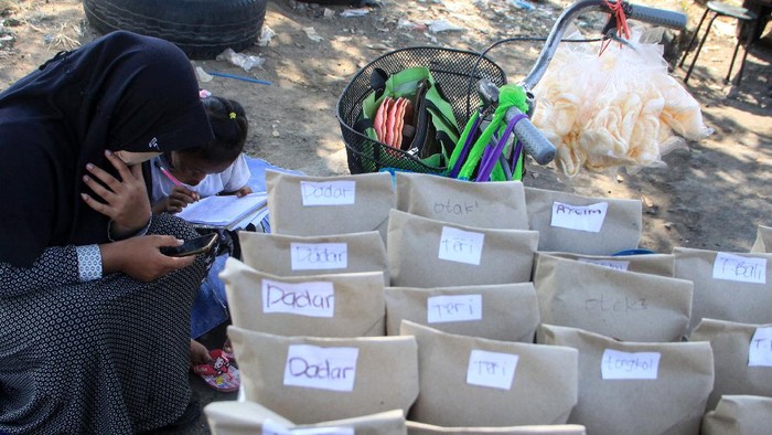 Pelajar kelas VIII MTs Darul Ulum, Sovi Dwi Aprilia (kiri) bersama adiknya, Tri Wahyu, yang masih kelas I SD belajar sambil berjualan nasi bungkus di pinggir jalan kawasan Delta Sari, Waru, Sidoarjo, Jawa Timur, Selasa (28/7/2020). Sovi berjualan nasi untuk membantu orangtuanya sekaligus mencari tambahan untuk membeli paket data internet agar bisa belajar secara daring. ANTARA FOTO/Umarul Faruq/foc.