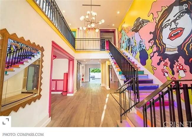 Rumah dua lantai ini dihubungkan dengan anak tangga warna-warni. Pada salah satu bagian dindingnya terdapat lukisan mural, juga dikreaskan dengan cat beraneka warna. Foto: Compass.com