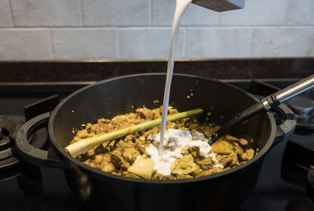 woman hand stirs in a pan on the gas stove with indonesian rendang, a stew with beef