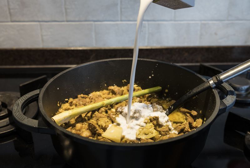 1134019109 woman hand stirs in a pan on the gas stove with indonesian rendang, a stew with beef