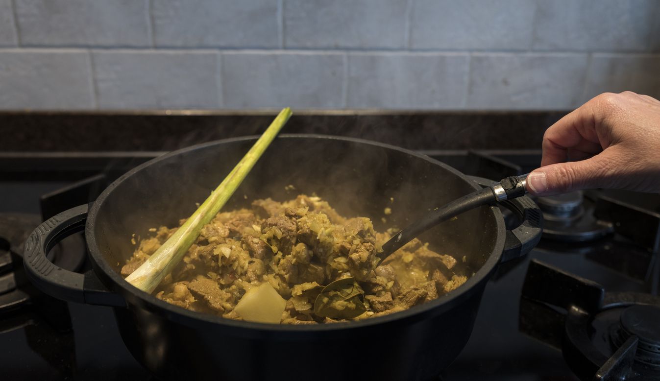woman hand stirs in a pan on the gas stove with indonesian rendang, a stew with beef