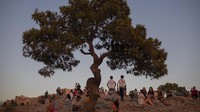 Wisatawan duduk di puncak bukit Areopagus, di depan bukit Acropolis, di Athena.  