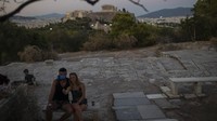 Sepasang kekasih mengabadikan diri mereka dengan ponsel di atas bukit Areopagus.  